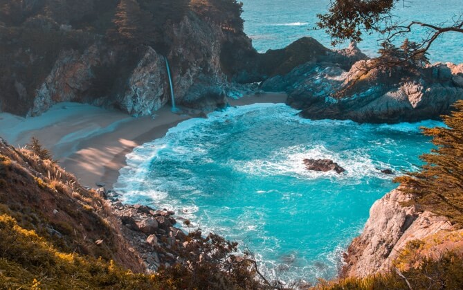 A secret beach, sheltered by cliffs, with bright blue water.